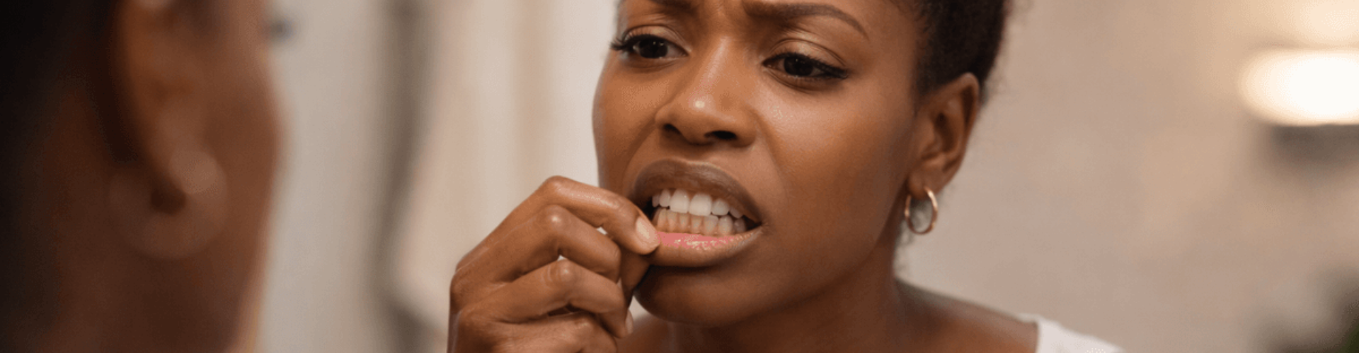 Woman pulling down lip to see gums in mirror.